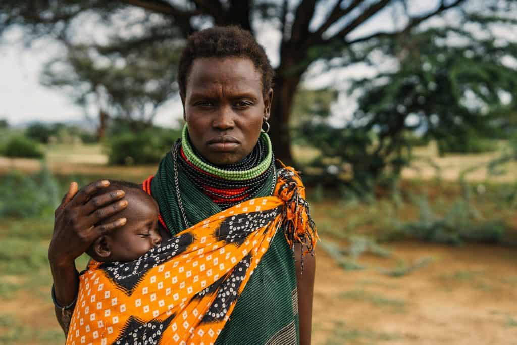 An African woman from Kenya holding her baby against a green landscape