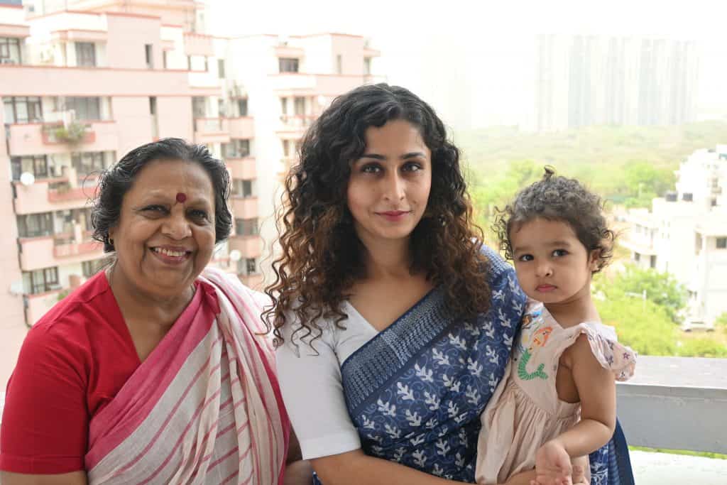 Trisha Mahajan holding her daughter and standing beside her mother. 