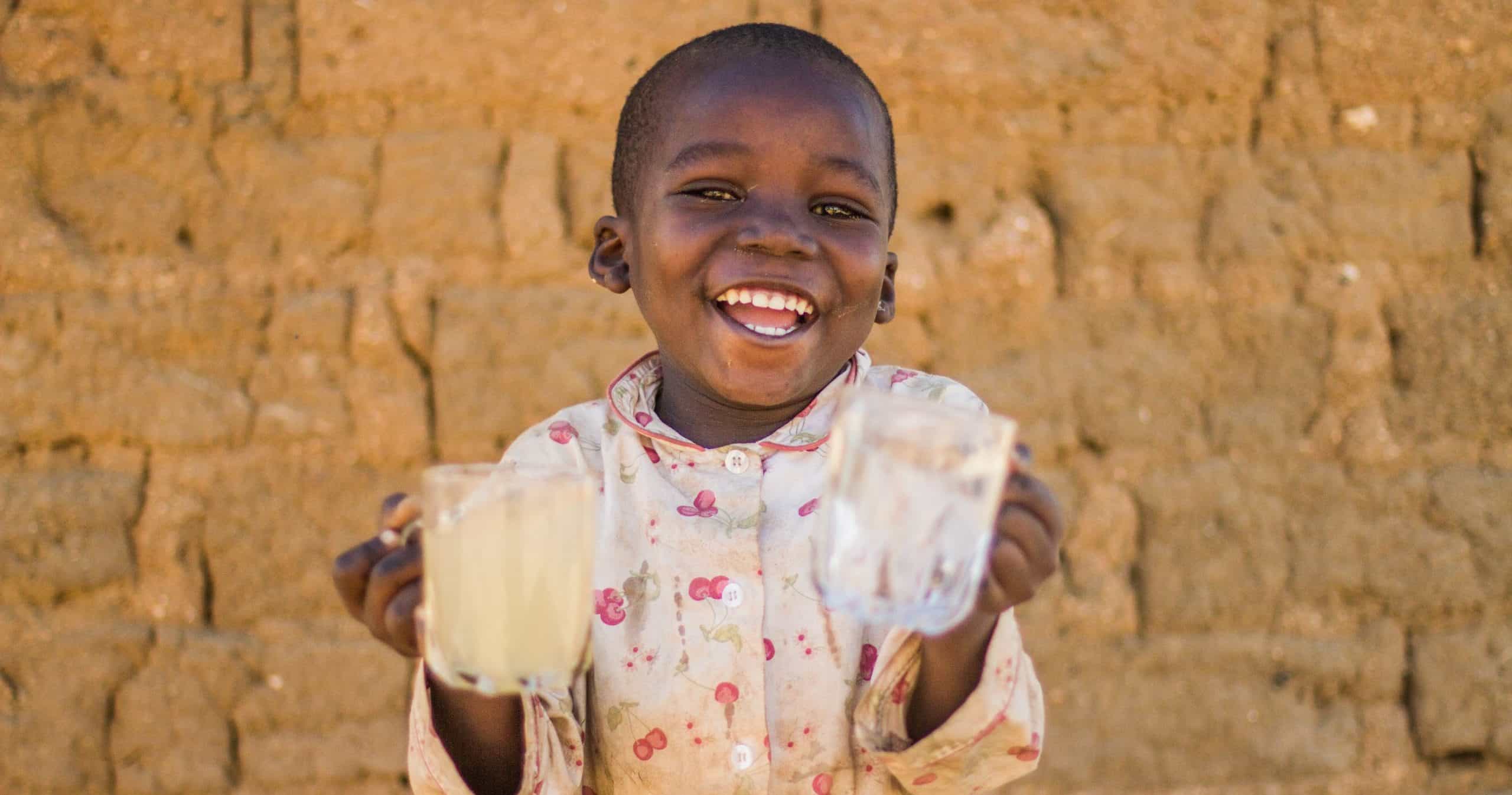 Smiling young girl holding two glasses of water. one with clean water and one with dirty water.