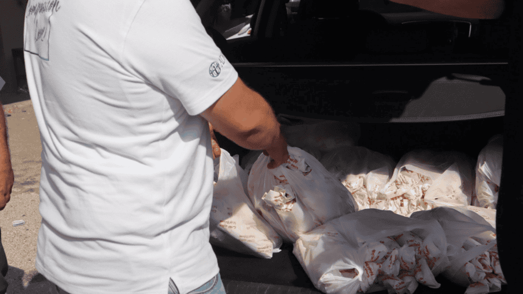 A man in a white ADRA shirt stands by open trunk full of bags of food