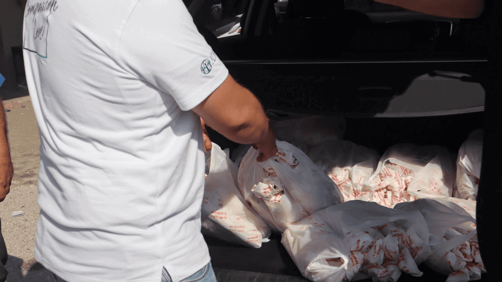 A man in a white ADRA shirt stands by open trunk full of bags of food