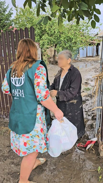 An ADRA Volunteer talks to an elderly woman, whose face is blurred.