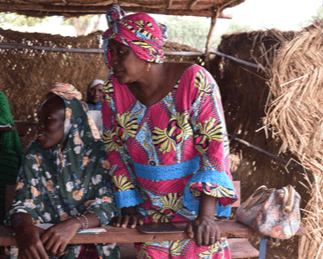 Mali Adult Literacy Program. Woman from Mali in a open air classroom. She is wearing a pink print dress and bandana