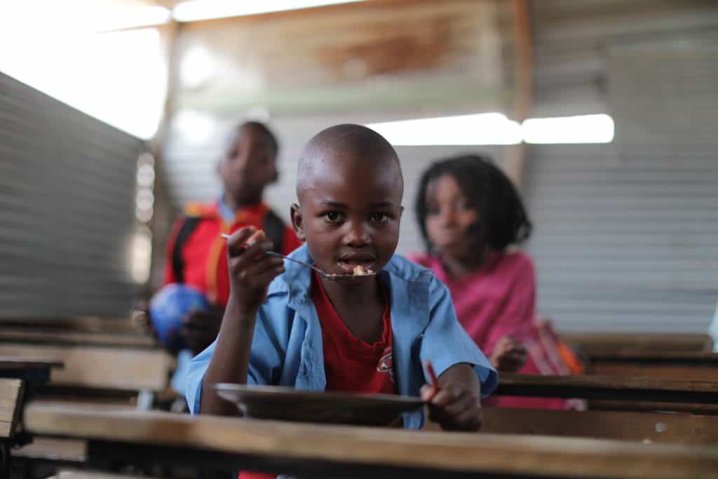 An African boy eating a nutritious meal in his school classroom as part of ADRA's School Feeding Initiative (SFI) project