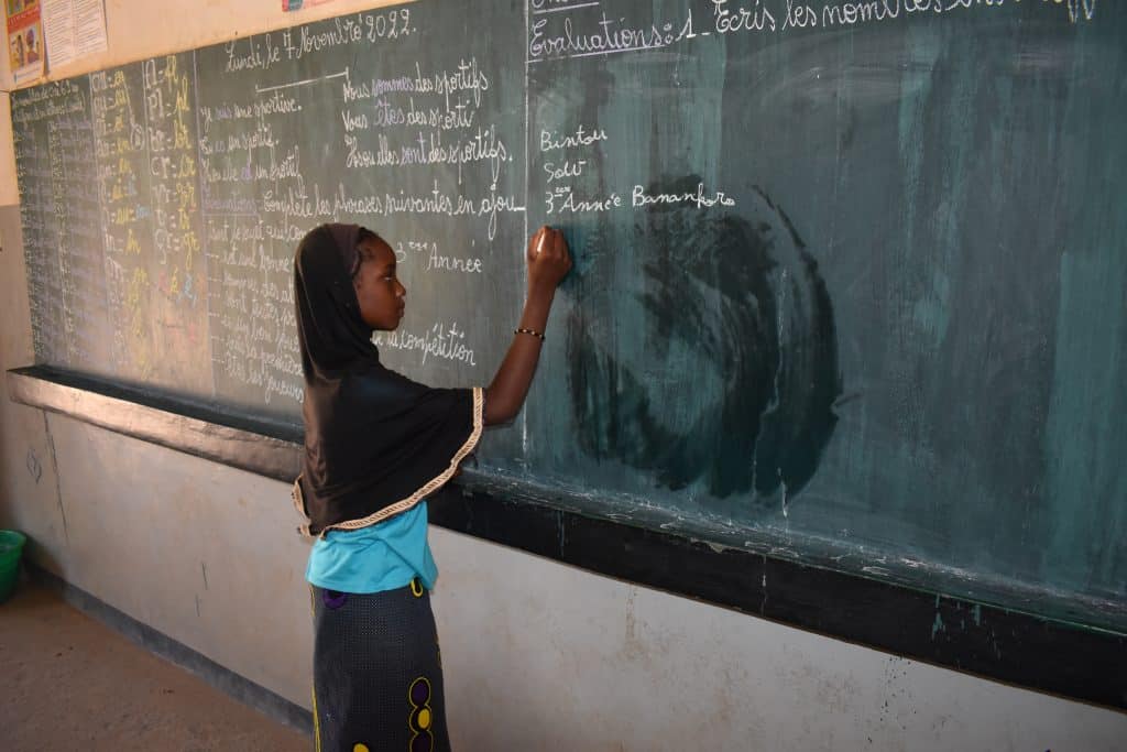 A young school girl writing on a blackboard in a classroom in Mali as part of ADRA's Education in Emergencies (EiE) project.