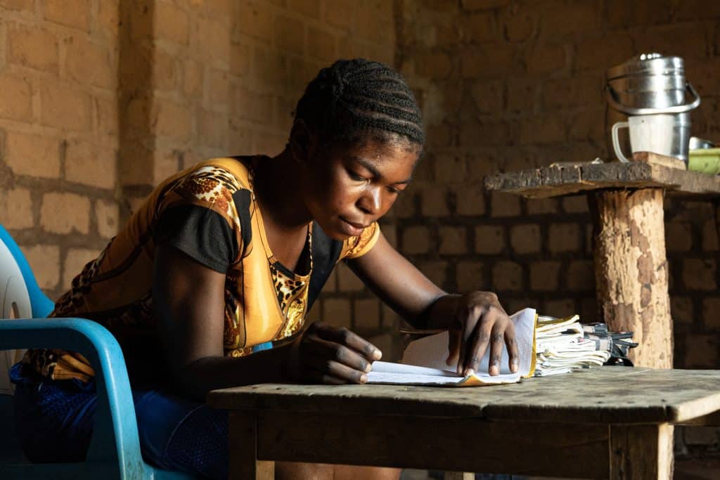 Denise Nduaya, a 16-year-old in Nfuanka DRC sits at a table writing in a notebook