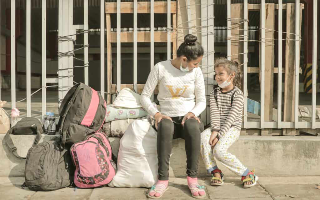 In Colombia, a mother and her daughter sit on a railing together. Migrants. Their life and possessions are beside them in bags.