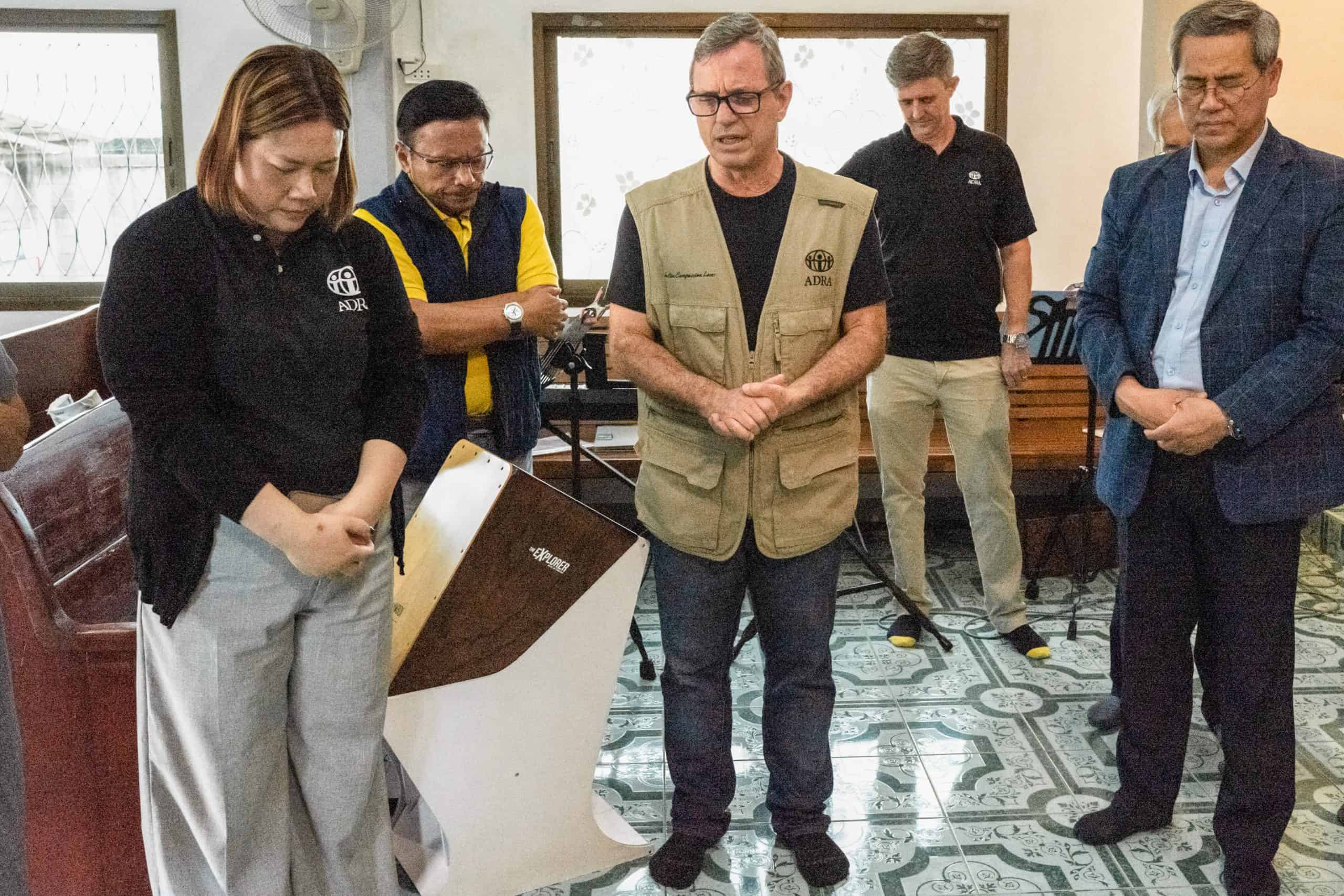 Paulo, a Brazilian man, and members from ADRA Thailand standing in a circle. Paulo is praying.