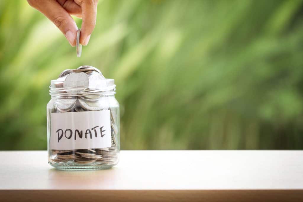 A donation jar labeled "Donate" with coins being added, symbolizing charitable giving and support.