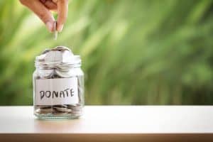A donation jar labeled "Donate" with coins being added, symbolizing charitable giving and support.