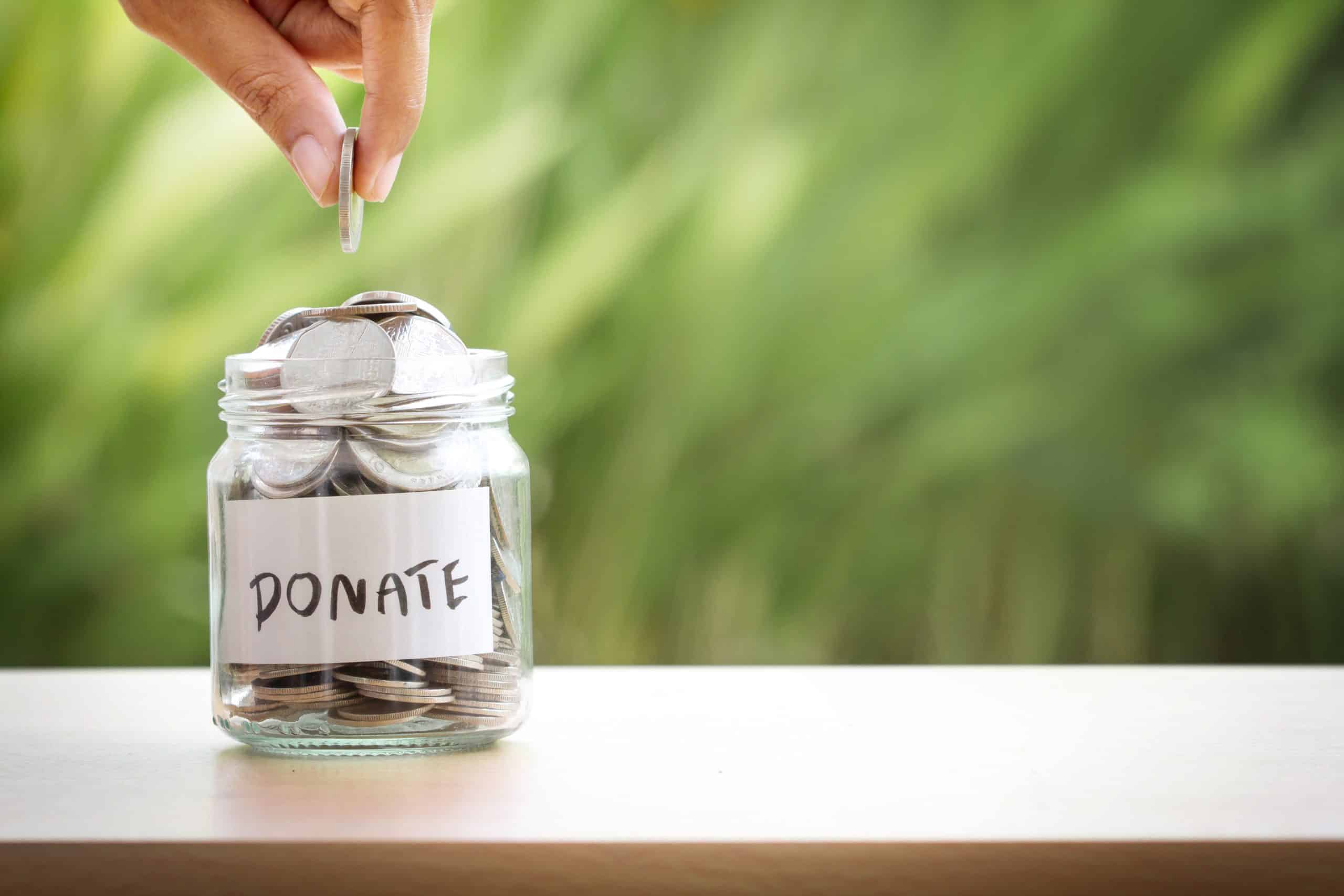 A donation jar labeled "Donate" with coins being added, symbolizing charitable giving and support.