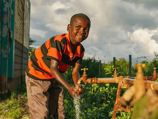 Washing hands at a water tap outdoors in a rural setting.