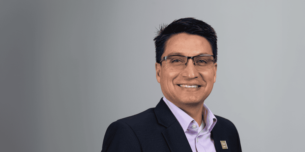 A smiling man in a navy suit and glasses, representing ADRA International's humanitarian work.