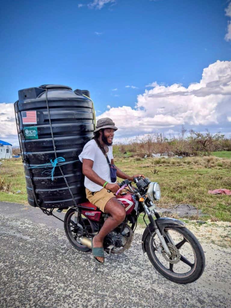 Volunteer delivering water on a motorcycle in a rural area for emergency relief efforts.