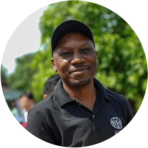 ADRA International volunteer smiling outdoors in a black polo shirt with logo, supporting community.