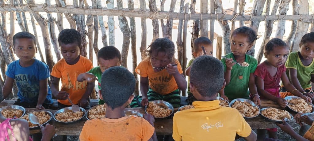 Children eating nutritious meal outdoors in a community setting for poverty alleviation.