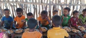 Children eating nutritious meal outdoors in a community setting for poverty alleviation.