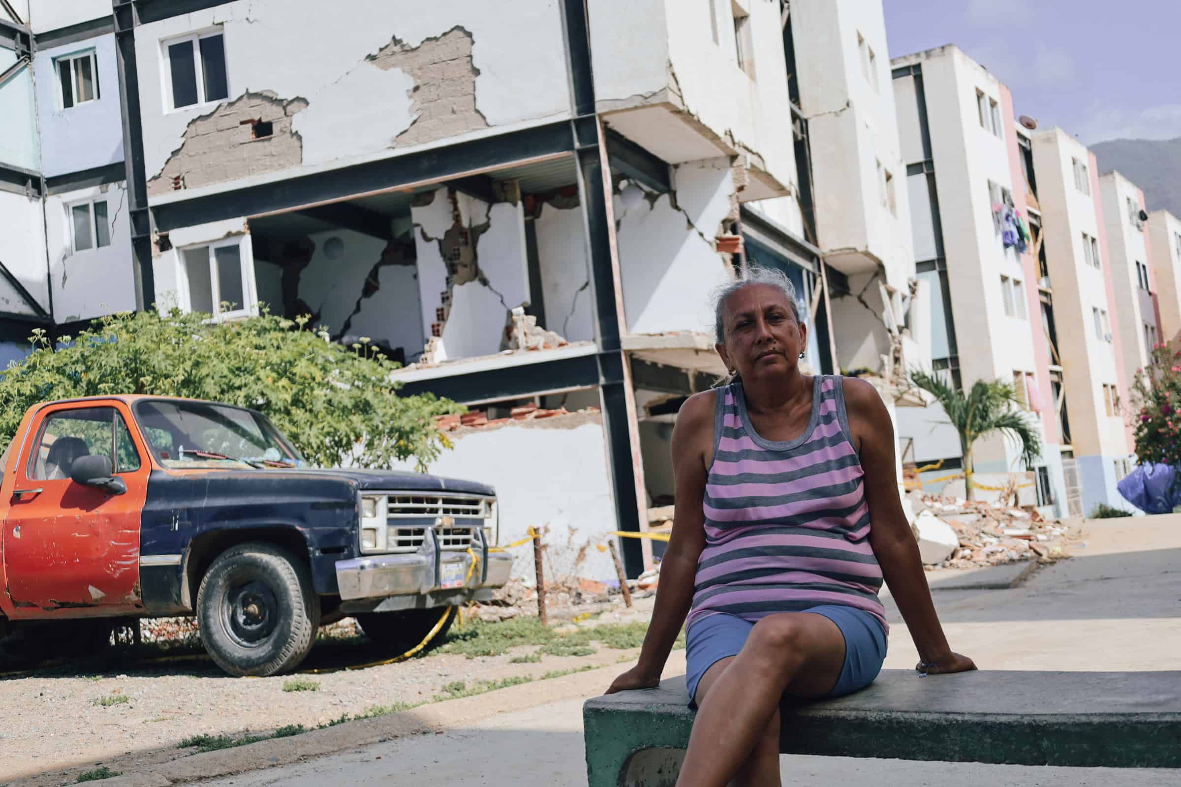 Woman sitting near damaged building after disaster in an urban area.