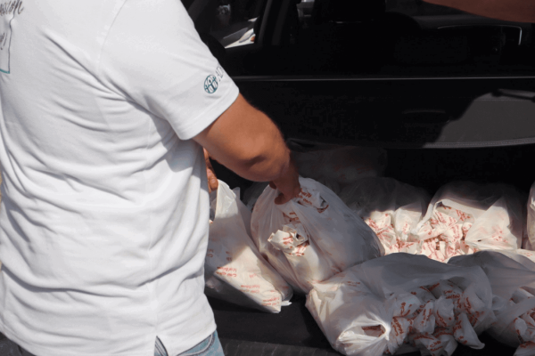 A man in a white ADRA shirt stands by open trunk full of bags of food